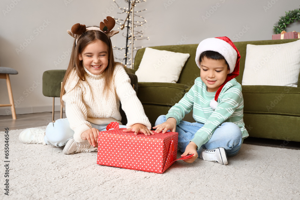 Cute little children unwrapping Christmas gift at home