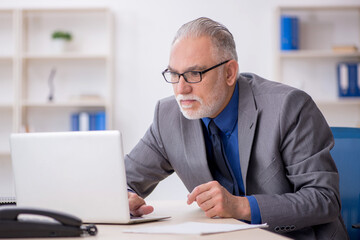 Wall Mural - Old male employee sitting at workplace