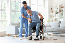 Male Nurse Helping Senior Man With Stick To Stand Up At Home