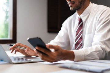 Wall Mural - Businessman researching data on smartphone and typing on laptop while analyzing strategy of startup