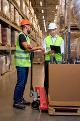 two men warehouse workers with hand pallet jack lift stand having talk, temwork. hand pallet truck and male mover. Workers in uniform with cargo cart. Delivery, logistic and shipping cargo