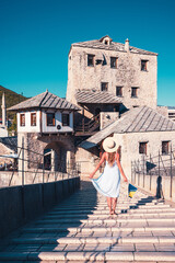 Wall Mural - Woman tourist in white dress and hat crossing old bridge in Mostar- Bosnia