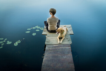 Wall Mural - Female with a labrador dog on a wooden fishing bridge enjoying peaceful warm water view.