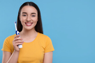 Wall Mural - Happy young woman holding electric toothbrush on light blue background, space for text