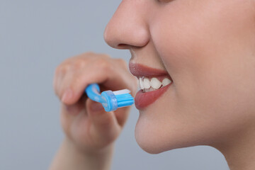 Wall Mural - Woman brushing her teeth with plastic toothbrush on light grey background, closeup. Space for text