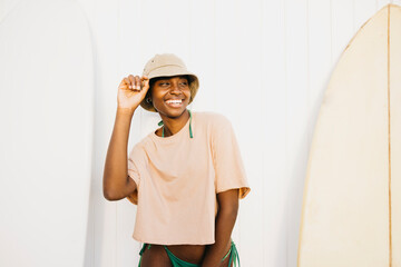 Wall Mural - Portrait of a cheerful young black woman  standing on a white wall with their surfboards after a day off at the beach.