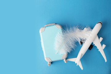 Airplane, luggage suitcase, and feather on a blue background, the easy elegance of flight