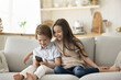 © fizkes - Little siblings spend time at home sit on couch with mobile phone, play video games for children, use on-line application, watch funny videos. Young gen and modern tech overuse, bad habit, addiction
