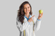 © Prostock-studio - Cheerful young lady doctor in uniform pointing finger on apple isolated on light grey background, smiling at camera