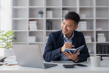 Wall Mural - Handsome Asian businessman take notes and with laptop in the office.