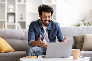 Wall Mural - Young Smiling Indian Man Making Video Call On Laptop At Home