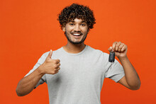 Young smiling happy fun Indian man he wearing t-shirt casual clothes hold in hand car key fob keyless system show thumb up isolated on orange red color background studio portrait. Lifestyle concept.