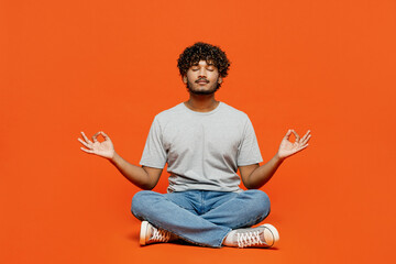 Wall Mural - Full body young happy spiritual Indian man wears t-shirt casual clothes sit hold spreading hands in yoga om aum gesture relax meditate try to calm down isolated on orange red color background studio.