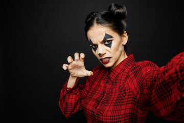 Wall Mural - Young woman with Halloween makeup face art mask wears clown costume red dress do selfie shot pov mobile cell phone isolated on plain solid black background studio portrait Scary holiday party concept