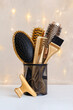Hairdressing gold combs, brush and scissors in a stand. Accessories for a hair salon on the background of Christmas lights.