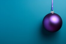 Purple Christmas Ball On Purple Ribbon Hanging On Blue Background With Copy Space