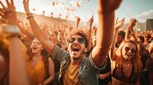 Delighted Young Male In Sunglasses With Mouth Opened Looking At Camera While Standing Among Cheering Crowd Of Audience, Attending Music Festival And With Hands Raised Showing Peace Sign Gesture 