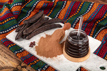 Carob Pods And Carob Beans. Dry Carob Pods And Carob Powder Over Wooden Background. Organic Healthy Ingredient For Vegan Vegetarian Food And Drinks, Close Up.
