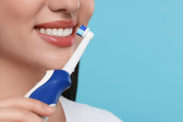 Wall Mural - Woman brushing her teeth with electric toothbrush on light blue background, closeup. Space for text