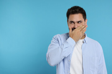 Wall Mural - Embarrassed man covering mouth on light blue background. Space for text