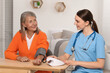 © New Africa - Young healthcare worker measuring senior woman's blood pressure at wooden table indoors