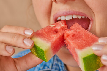 Close-up of two pieces of watermelon, which a Caucasian woman puts into her mouth. Front three-quarter view. Low angle view.