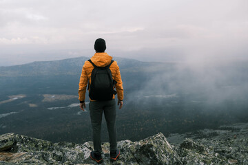  tourist with a backpack stands on the top of the mountain with his back and enjoys the landscape.Active lifestyle