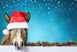 A horse or pony in a santa claus hat peeks behind a banner with new year decorations on a blue background. New year poster layout concept with empty space for product placement or text.