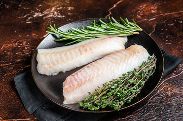 Wall Mural - Raw cod loin fillet steaks with herbs on plate. Dark background. Top view