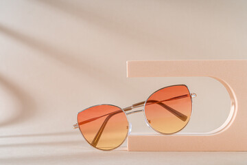 Fashionable sunglasses with color lenses in metallic frame on podium on beige background. Women's Trendy sunglasses still life in minimal style. Eyewear fashion. Optic store discount, sale. Copy space