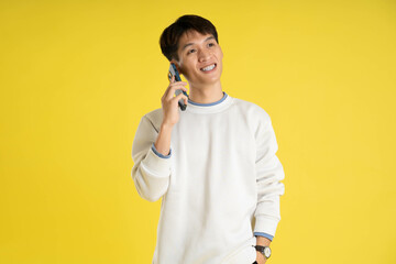 Wall Mural - portrait of young Asian man wearing sweater and using phone on yellow background