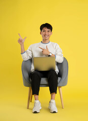 Wall Mural - full body of young Asian man wearing sweater and using latop on yellow background