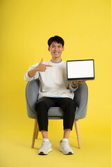 Canvas Print - full body of young Asian man wearing sweater and using latop on yellow background