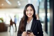 © Usablestores - Cheerful Asian Businesswoman Holding Cellphone and Smiling at Camera