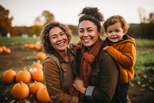 Family Portrait Of A Lesbian Couple Holding Their Toddler Kid In A Pumpkin Patch During Autumn. Halloween And Thanksgiving Activities For Families. LGBTQ Diverse Family.