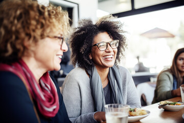 Wall Mural - Happy smiling middle aged female friends sitting in a café laughing and talking during a lunch break