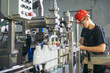 Production line worker or technologist in uniform working in chemical industry and checking quality of liquid soap.