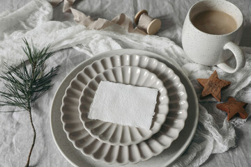 Wall Mural - Christmas still life. Blank business card, invitation mockup on ceramic plate. Wooden stars and pine tree branches on white linen tablecloth. Cup of coffee, winter breakfast. Festive holiday flat lay