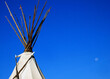 Top of a Native American tip or wigwam stands against a bright, blue sky.