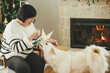 © sonyachny - Happy senior woman playing with adorable white dog in stylish festive christmas living room. Beautiful woman enjoying cozy fireplace with cute pet on background of decorated christmas tree