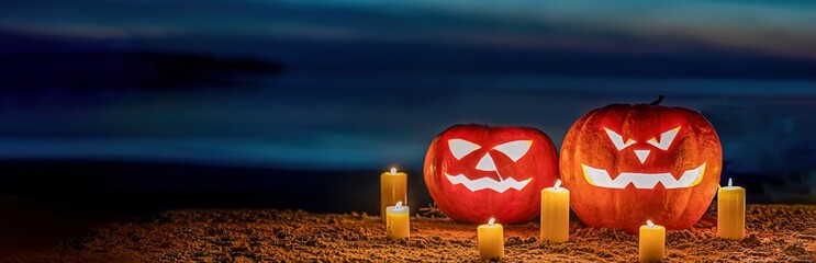 a pair of halloween pumpkin lanterns sitting on a sandy beach at night.