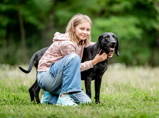 Wall Mural - Preteen girl hugging golden retriever dog sitting at nature together. Cute child kid petting purebred pet doggy labrador in park at summer