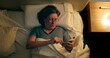 © Marco - Older woman lies in bed messaging using smartphone device before sleep