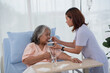Asian nurse feeding breakfast to elderly female patient on bed in hospital ward
