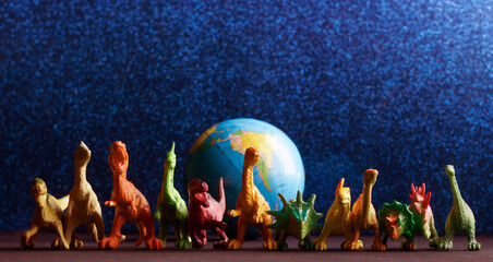 Toy dinosaurs protect the globe on a shimmering blue background. Concept of protecting planet Earth and preventing alien invasion. Creativity in children's play. Photo