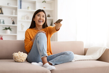 Wall Mural - Happy young asian lady watching TV and eating popcorn