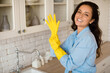 © Prostock-studio - Portrait of joyful woman putting on rubber gloves, ready to tidy house or washing dishes standing in kitchen, free space