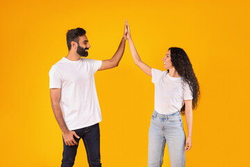 Wall Mural - Cheerful Arab Young Couple Giving High Five Over Yellow Background