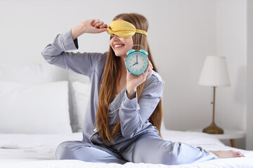Wall Mural - Happy young woman in pajamas with alarm clock on bed at home