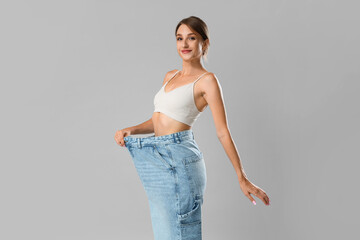 Canvas Print - Beautiful young woman in loose jeans on grey background. Weight loss concept